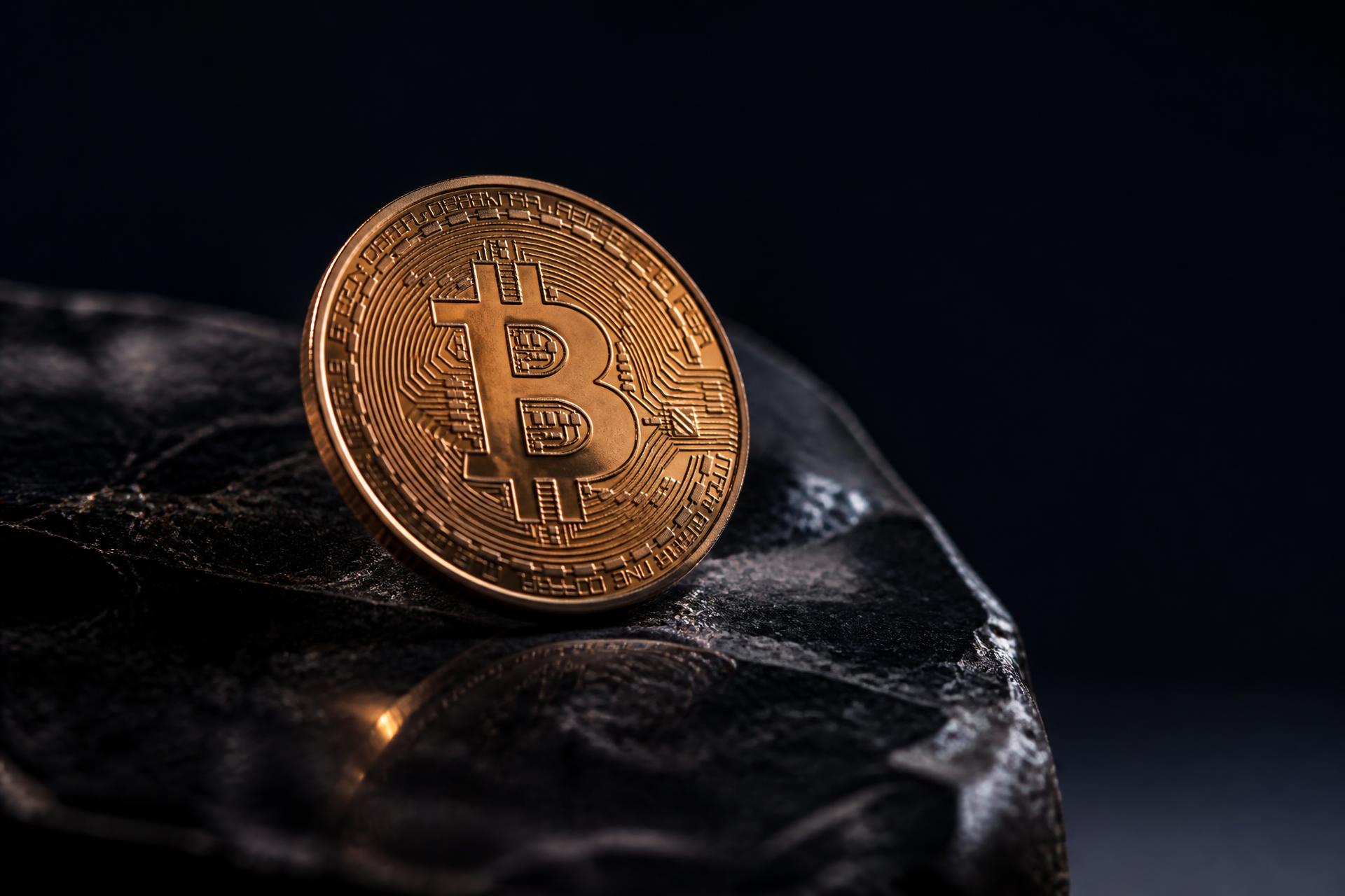 A single physical Bitcoin coin rests on polished obsidian stone, lit dramatically from above with copper highlights on its rim.